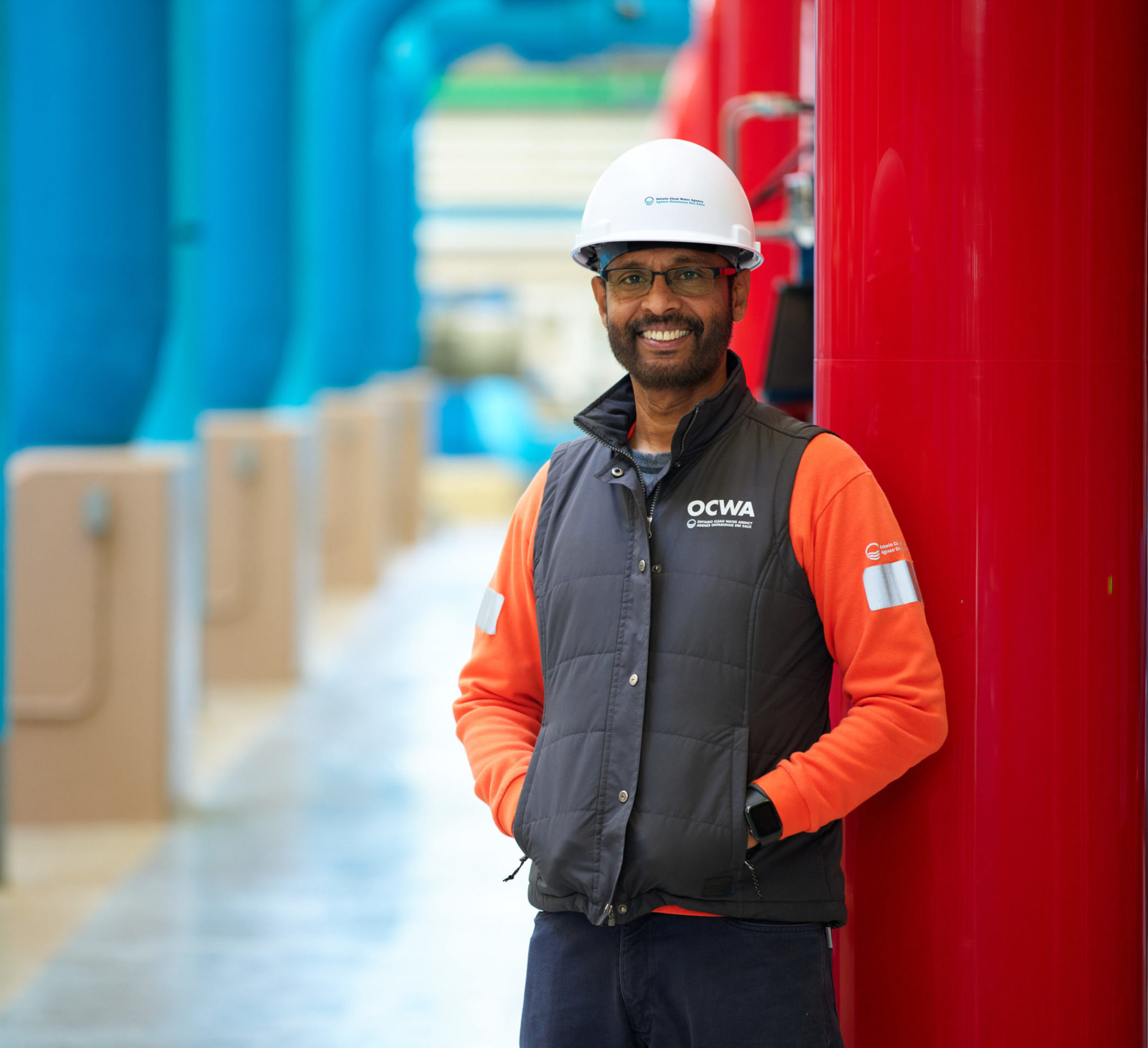 OCWA employee in protective gear standing inside water treatment plant and smiling at the camera