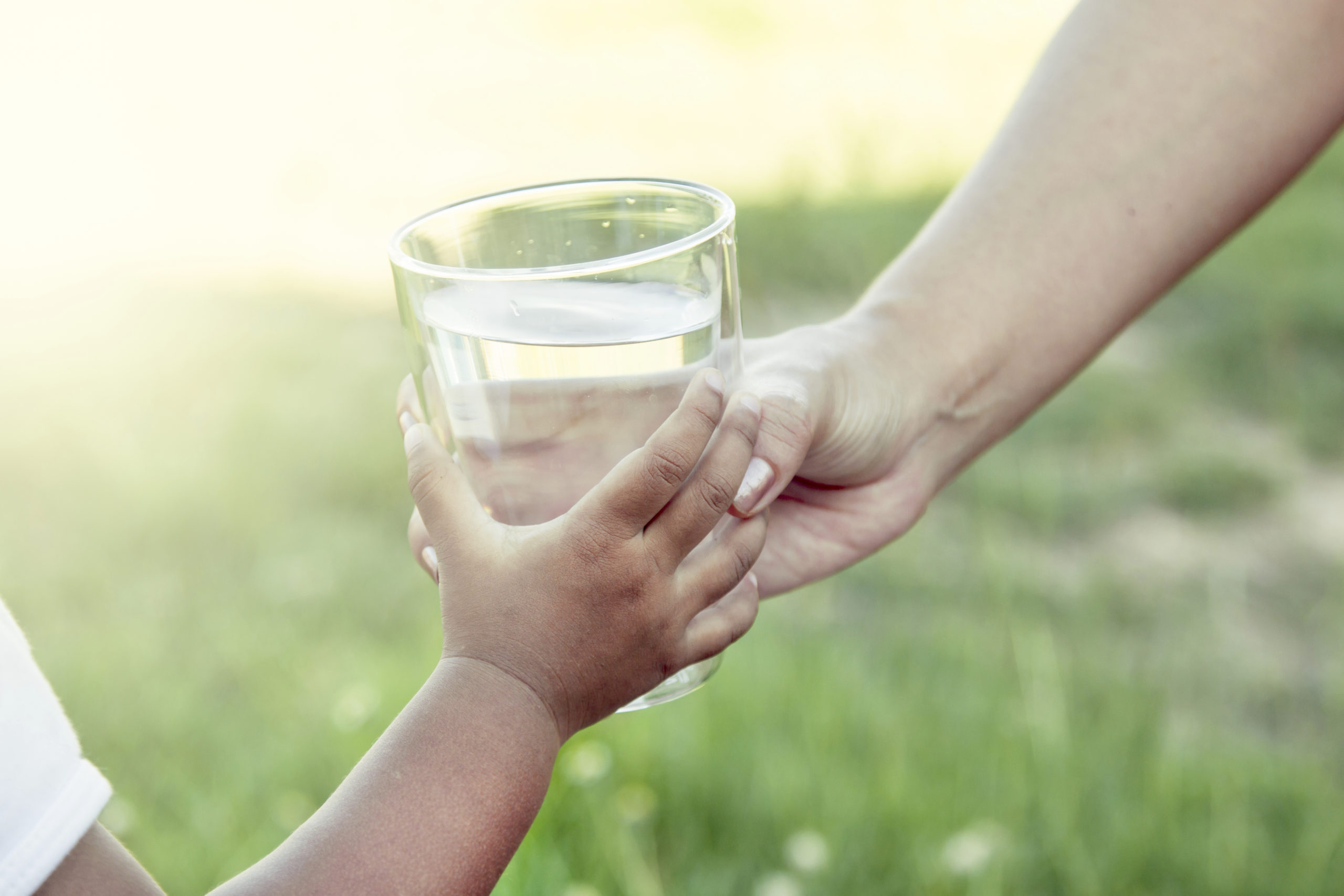 Woman hand giving glass of fresh water to child in the park,soft color filter