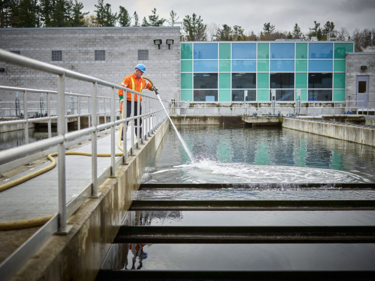 Exploitant de l’AOE en tenue de protection qui arrose au boyau un plan d’eau à l’extérieur d’une usine de traitement des eaux usées.