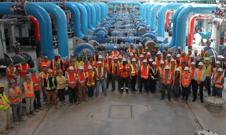 Une grosse équipe d’exploitants de l’AOE en tenue de protection sourient à la caméra dans une usine de traitement des eaux.