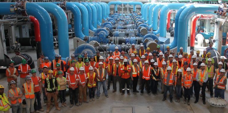 Large team of OCWA operations staff wearing protective gear inside water treatment plant looking up at camera and smiling